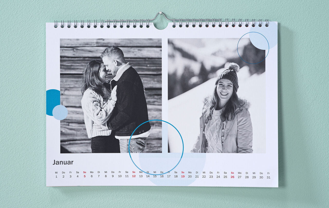 Kalendar sa zimskim crno-bijelim fotografijama i kružnim clip art-ovima u plavoj boji visi na menta zelenom zidu.