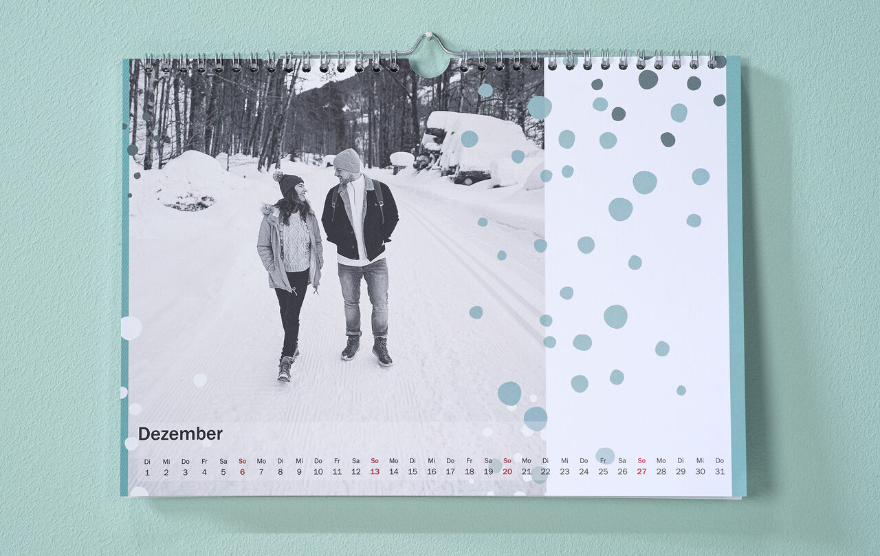Kalendar sa zimskom fotografijom para i točkastim clip art-om visi na zidu.